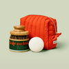 Red quilted pouch, white bath bomb, and jar with green label on a light beige background