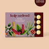 Kate McLeod 'The Pebble' solid bath and shower oil in a limited edition box, featuring botanical illustrations on a lavender background with pale yellow round bars visible in the tray, set against a warm beige background with a 'LIMITED EDITION' badge.