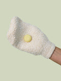 A hand wearing the Body Mitt with a Pebble on it against a ight green background.