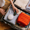 The Travel Bag, a poppy-orange quilted, zippered pouch, showed in a suitcase for travel.