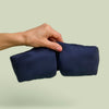 Hand holding Lunya Silk Sleep Mask up against a light green background.