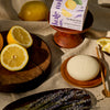 The New Summer Limited-Edition Lavender Lemonade Body Stone box styled next to the body stone, alongside fresh lemons and lavender.
