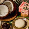 Kate McLeod Tonka Bean & Coconut lotion bar with packaging on a dish with ingredients and linens around
