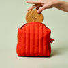 Person placing a Bamboo Canister into the poppy Travel Bag against a light green background.