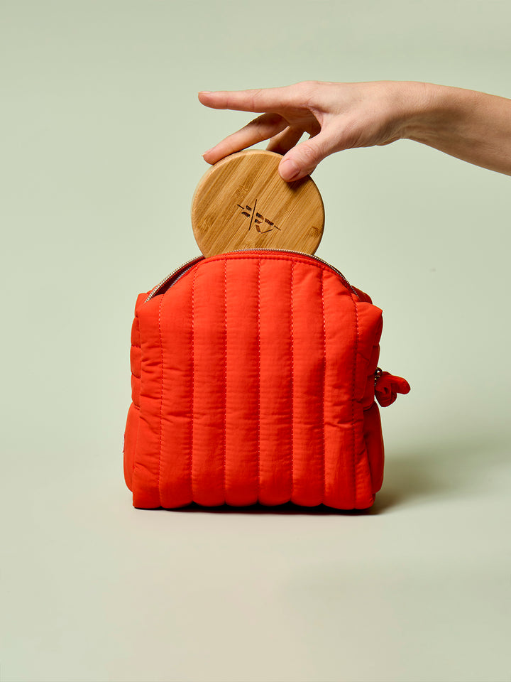 Person placing a Bamboo Canister into the poppy Travel Bag against a light green background.