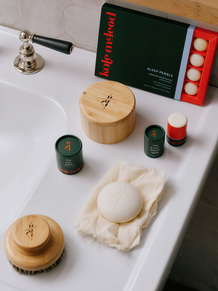 The Bamboo Canister styled on the surface of a bath alongside Kate McLeod's Body Brush, The Face Balm, The Everywhere Stick and Sleep Pebble