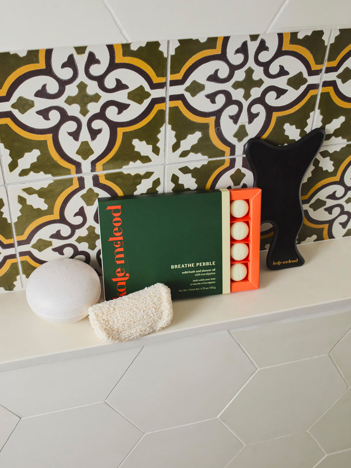 The body mitt folded neatly on the tiled bathroom counter paired alongside Kate McLeod's Breathe Pebble and Travel Case.