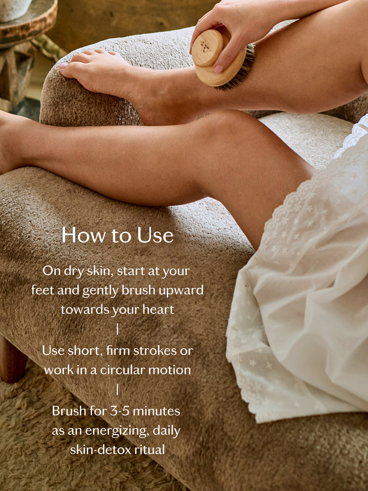 Woman sitting on a brown sofa exfoliating her skin with the dry brush and how to use text over the image.