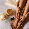 Person's legs and feet with the Kate McLeod reusable body stone canister, foot stone, and foot file on a white surface