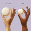Two hands holding a full-size and a mini-sized product against a light purple background