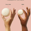 Two hands holding a full size and a mini version of a product against a pink background.