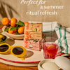 Summer limited edition Body Stones in a summer-themed setting with Travel Case, oranges, sunglasses, and a glass of iced tea on a wooden table. Perfect for a summer refresh.