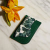 Face Gua Sha and green felt case on marble counter with yellow flowers.