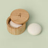 Bamboo Canister with lid that swings open pictured against green background with a Body Stone lotion bar nestled inside and another Body Stone next to it. Body Stones sold separately.