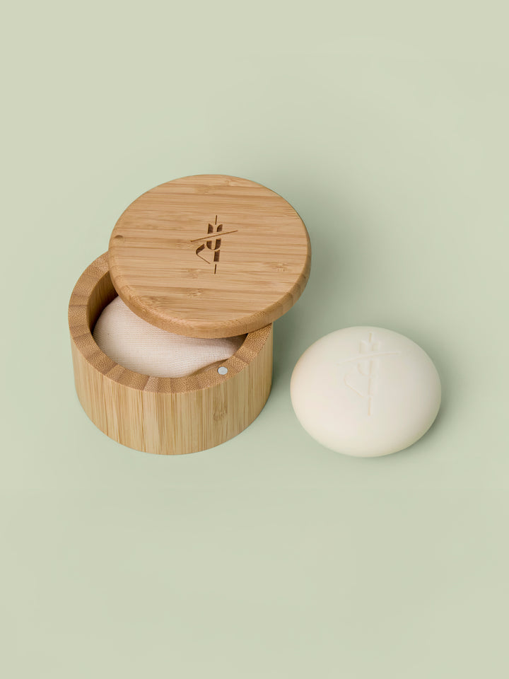 Bamboo Canister with lid that swings open pictured against green background with a Body Stone lotion bar nestled inside and another Body Stone next to it. Body Stones sold separately.