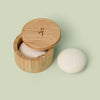 Bamboo Canister with lid that swings open pictured against green background with a Body Stone lotion bar nestled inside and another Body Stone next to it. Body Stones sold separately.