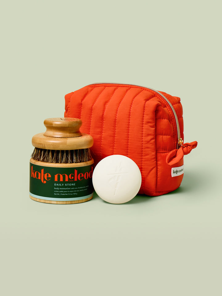 Red quilted pouch, white bath bomb, and jar with green label on a light beige background