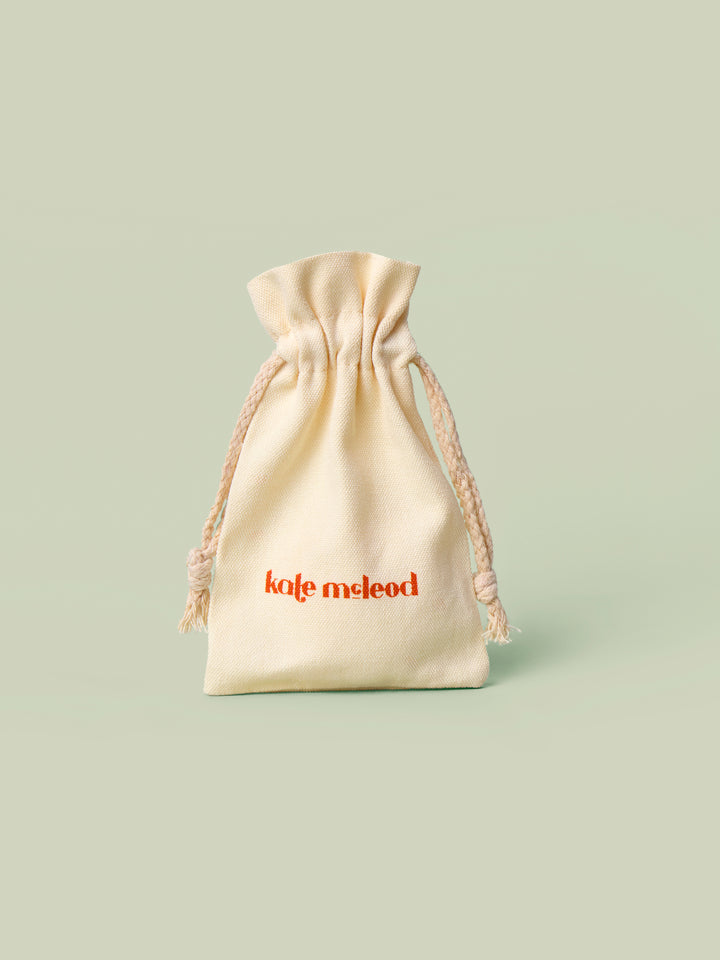 Beige drawstring canvas bag, the Mini Gift Bag, with 'Kate McLeod' logo on a light green background.