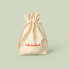 A beige drawstring bag with Kate McLeod logo, the Gift Bag, on a light green background