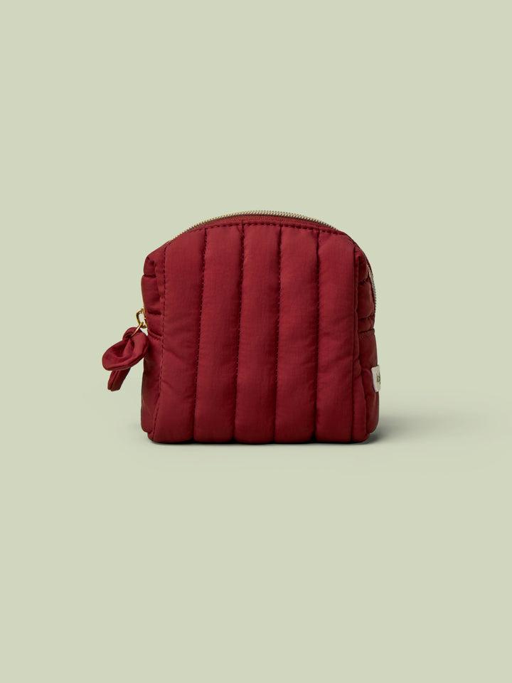 The Mini Travel Bag, a wine-red quilted zippered pouch, against a light green background.