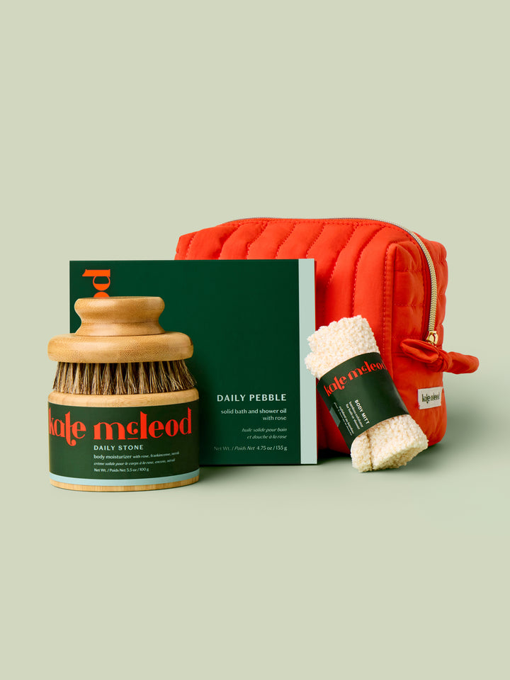 The Spa Gift set features a dry brush, daily pebble, body mitt and poppy-colored travel bag. The set is displayed on a light green background.