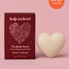 Heart-shaped lotion bar with packaging on a pink background