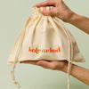 Large beige drawstring bag with Kate McLeod logo, the Large Gift Bag, held by hands against a light green background