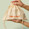 Large beige drawstring bag with Kate McLeod logo, the Large Gift Bag, held by hands against a light green background