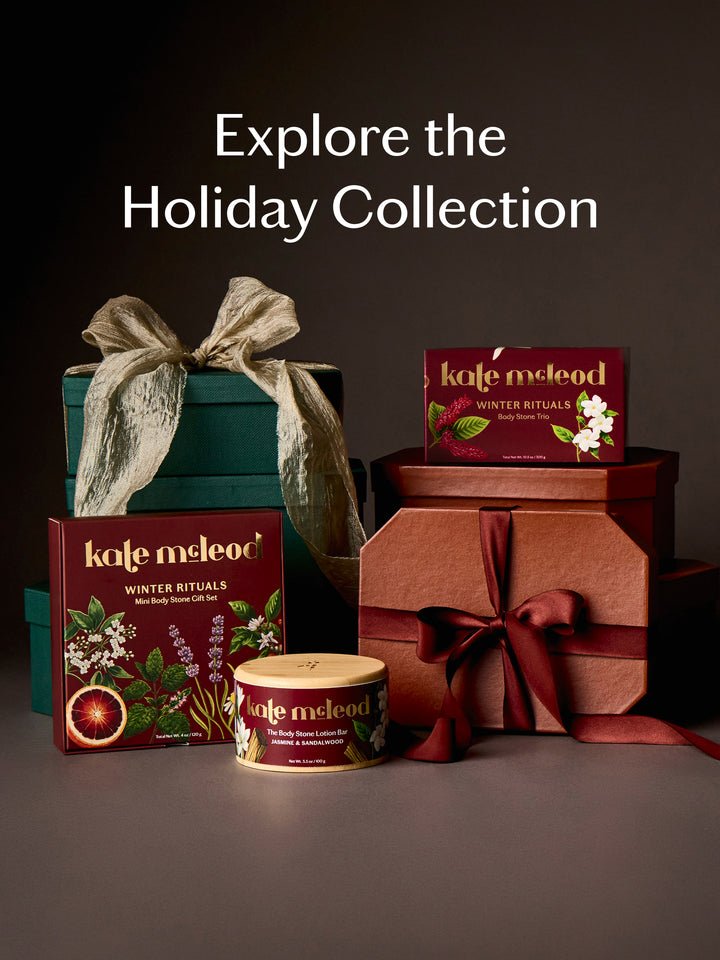 A holiday gift set display featuring multiple boxes and tins from kale meLeod Winter Rituals, arranged on a dark studio background with the text 'Explore the Holiday Collection' at the top.