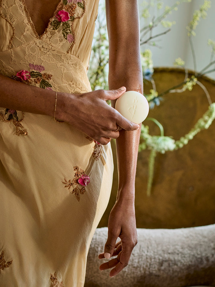 Person in a yellow floral dress holding a white Body Stone against her arm with a natural background.