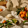 Kate McLeod Tangerine & Vanilla lotion bar on a stone plate with bowls full of oranges and vanilla flowers and vanilla bean stalks.