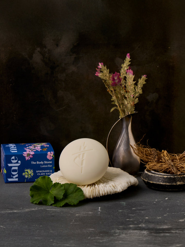 Lifestyle image of Spikenard & Clary Sage on a textured plate with packaging, spikenard in a silver ewer, and clary sage on a bronze plate.