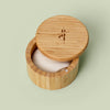 Bamboo Canister with lid that swings open pictured against green background with a Body Stone lotion bar nestled inside. Body Sones sold separately.