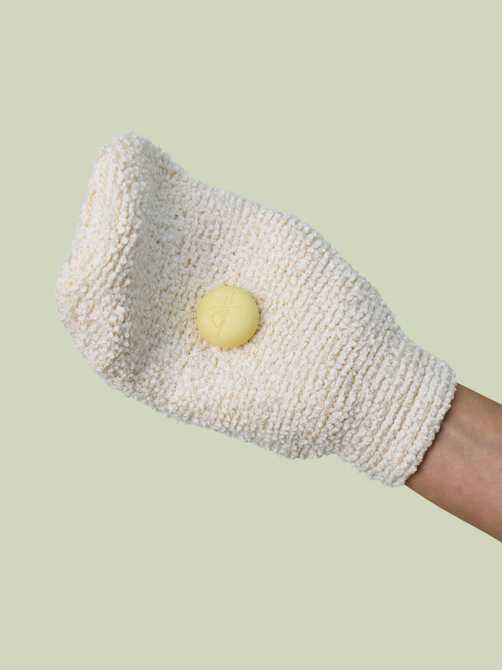 A hand wearing the Body Mitt with a Pebble on it against a ight green background.