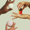 Three hands applying and holding the sleep stone mini, everywhere stick and travel case on a light green background. 