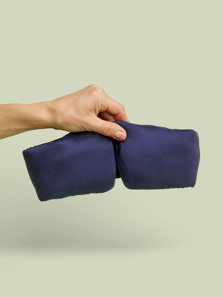 Hand holding Lunya Silk Sleep Mask up against a light green background.