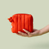 Hand holding Mini Travel Bag, a orange red poppy colored quilted zippered pouch, against a light green background.