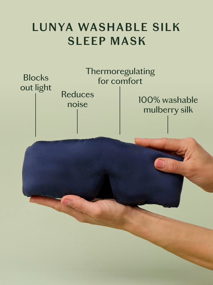 Lunya Washable Silk Sleep Mask held by a hand with features listed on a light green background. Blocks out light, reduces noise, thermoregulating comfort, 100% washable mulberry silk.