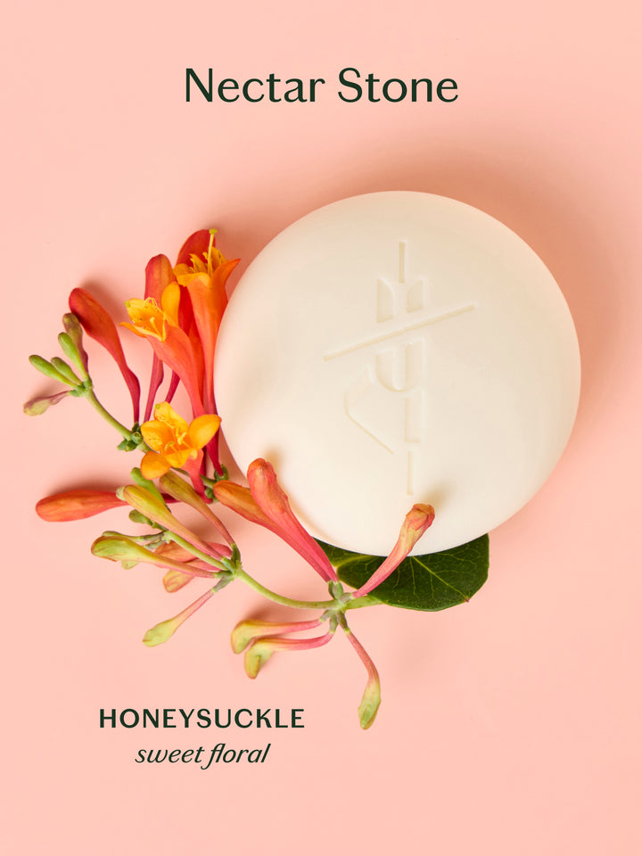 Nectar Stone Honeysuckle Body Stone Lotion Bar on a peach background with honeysuckle flowers. Sweet floral scent.