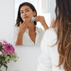 Woman the Gua Sha along her jawline in front of a mirror