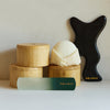 Bamboo canisters, a body sone, the foot file and the gua sha sit atop a white counter,