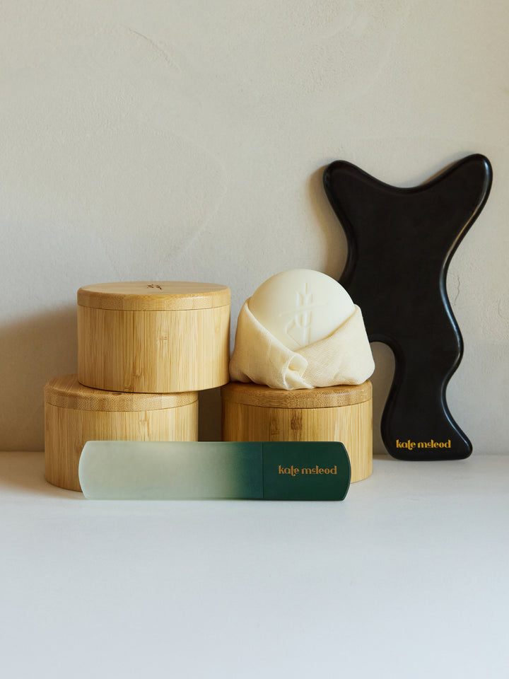 Bamboo canisters, a body sone, the foot file and the gua sha sit atop a white counter,