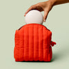 Person placing a Full-Size Travel Case into the poppy Travel Bag against a light green background.