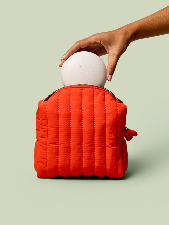 Person placing a Full-Size Travel Case into the poppy Travel Bag against a light green background.