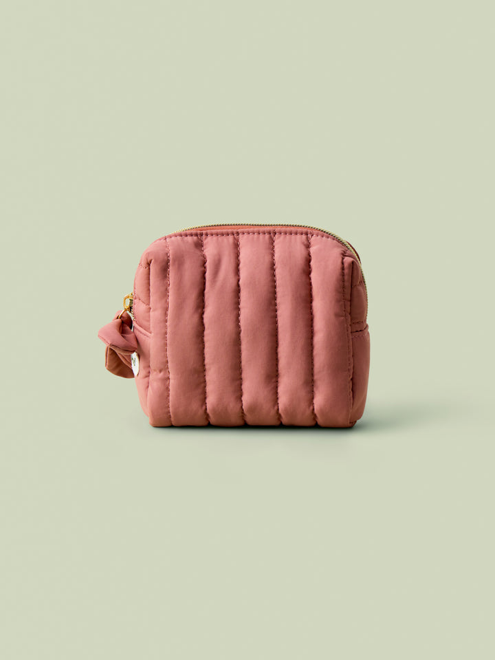 Blush quilted mini travel bag on a light green background