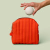 Packing the quilted travel bag in poppy orange color with the mini travel case on a light green background.