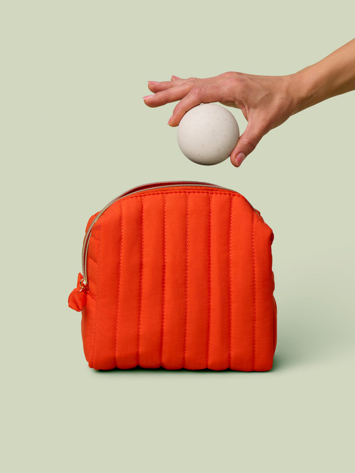 Packing the quilted travel bag in poppy orange color with the mini travel case on a light green background.