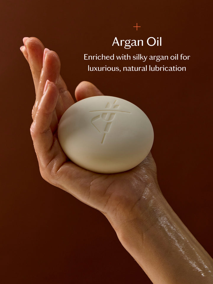 Hand holding a Sex Stone with argan oil text on a brown background