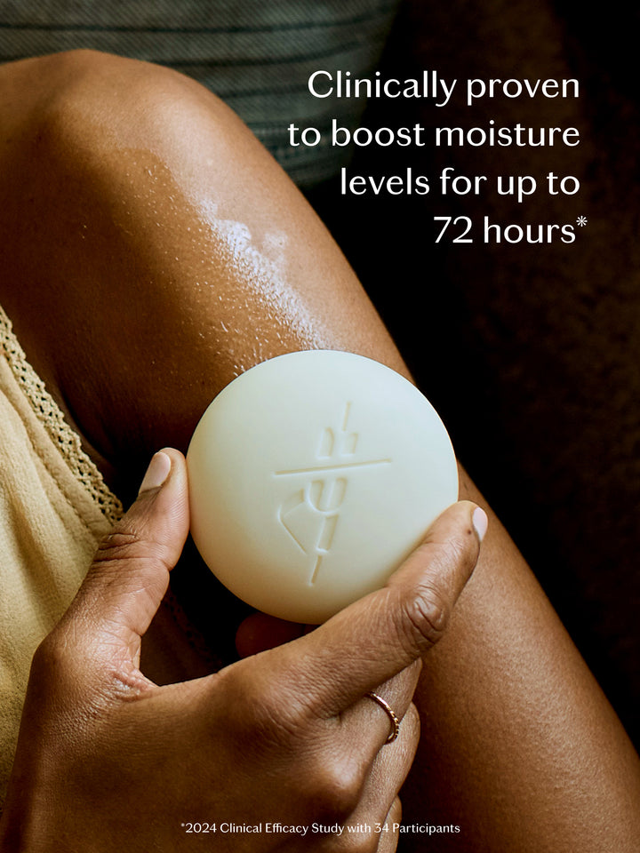 Hand holding a white Body Stone lotion bar against skin with text about clinical claim. Boosts moisture levels for up to 72 hours.