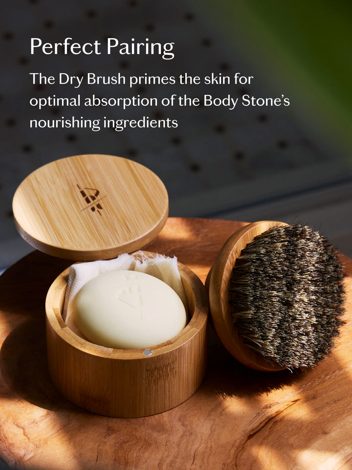 Bamboo canister sits atop a wooden table holding the body stone and the dry brush is propped up next to it. Text over the image shares why the two products are the perfect pairing.